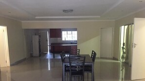 Amplia sala de estar con mesa y sillas de comedor, una cocina al fondo y una puerta a la derecha.