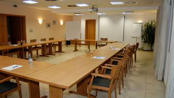 Ein Konferenzraum mit langen Tischen, Stühlen, einem Projektor, einer Tafel und einer Pflanze.