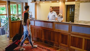 A reception area with a wooden counter, potted plants, and a view of the outdoors. - Landhotel Aschenbrenner (Freudenberg)