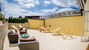 A sunlit outdoor seating area with wicker furniture and a yellow wall. - Landhotel Aschenbrenner (Freudenberg)