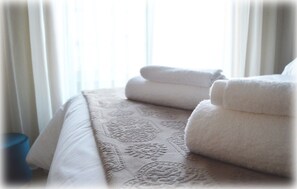 Cama bem arrumada com colcha estampada e toalhas brancas dobradas.