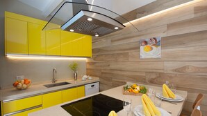 Una cocina moderna con armarios amarillos, horno empotrado y comedor con mesa para dos.