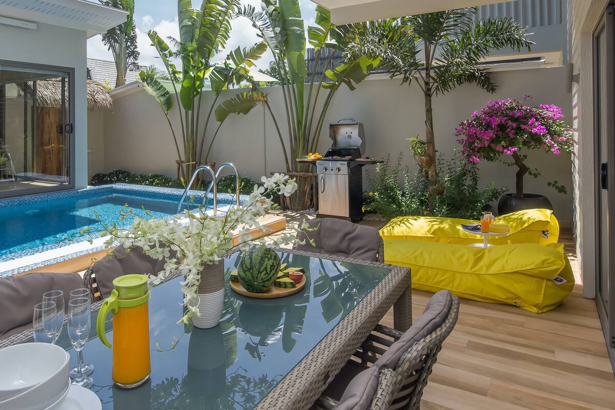 Uma área na piscina com mesa de vidro, cadeiras e churrasqueira.