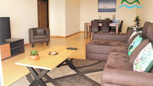 Una sala de estar con sofá, una mesa de centro, televisor, comedor con mesa y sillas, y una puerta.