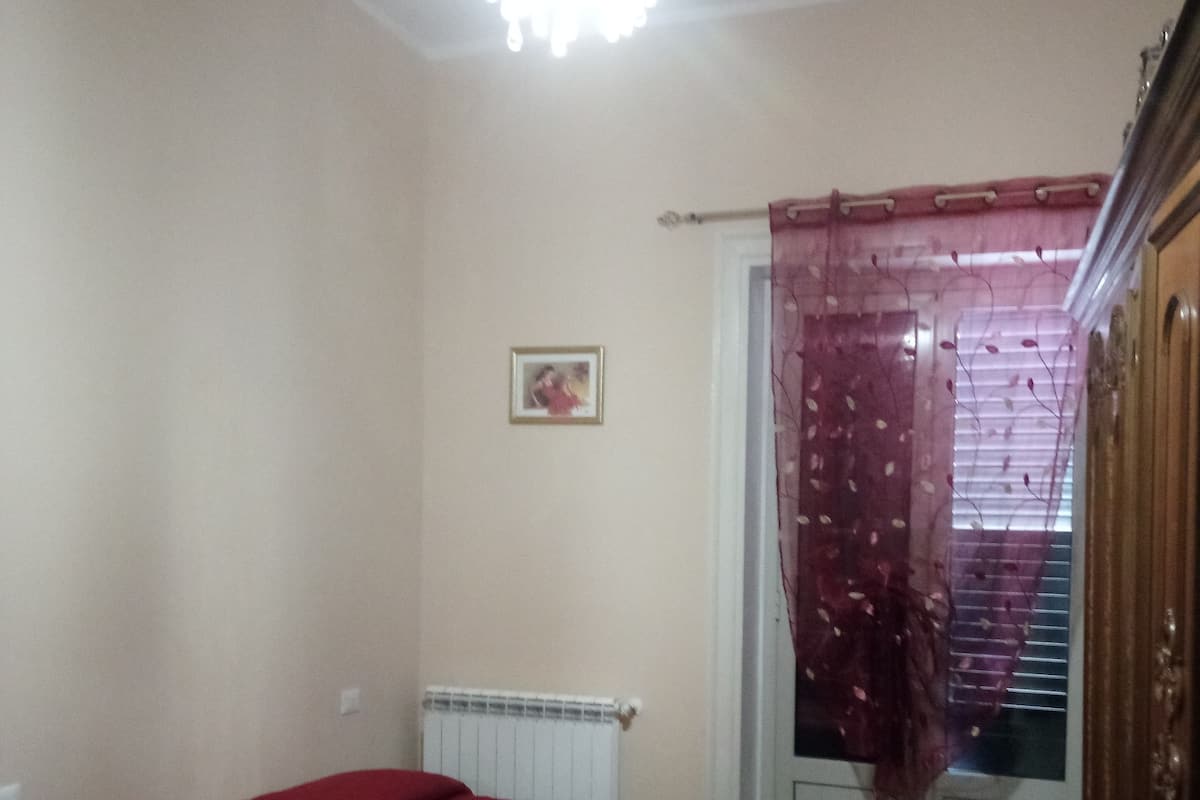 Een kamer met twee bedden, een radiator, een raam met gordijn en een foto aan de muur.