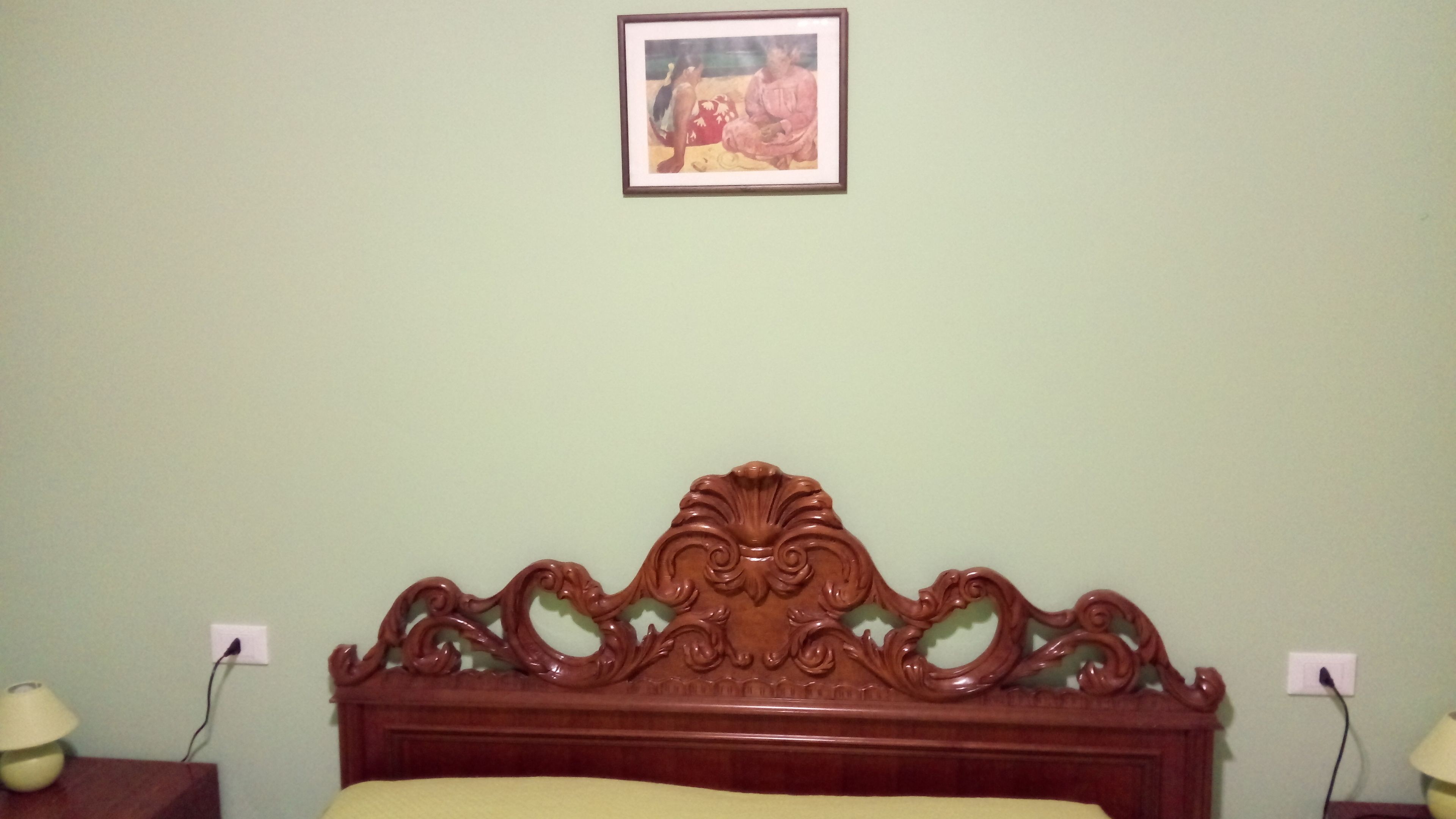A bedroom with a wooden headboard, a bed with a yellow bedspread, two bedside lamps, and a framed picture on the wall.