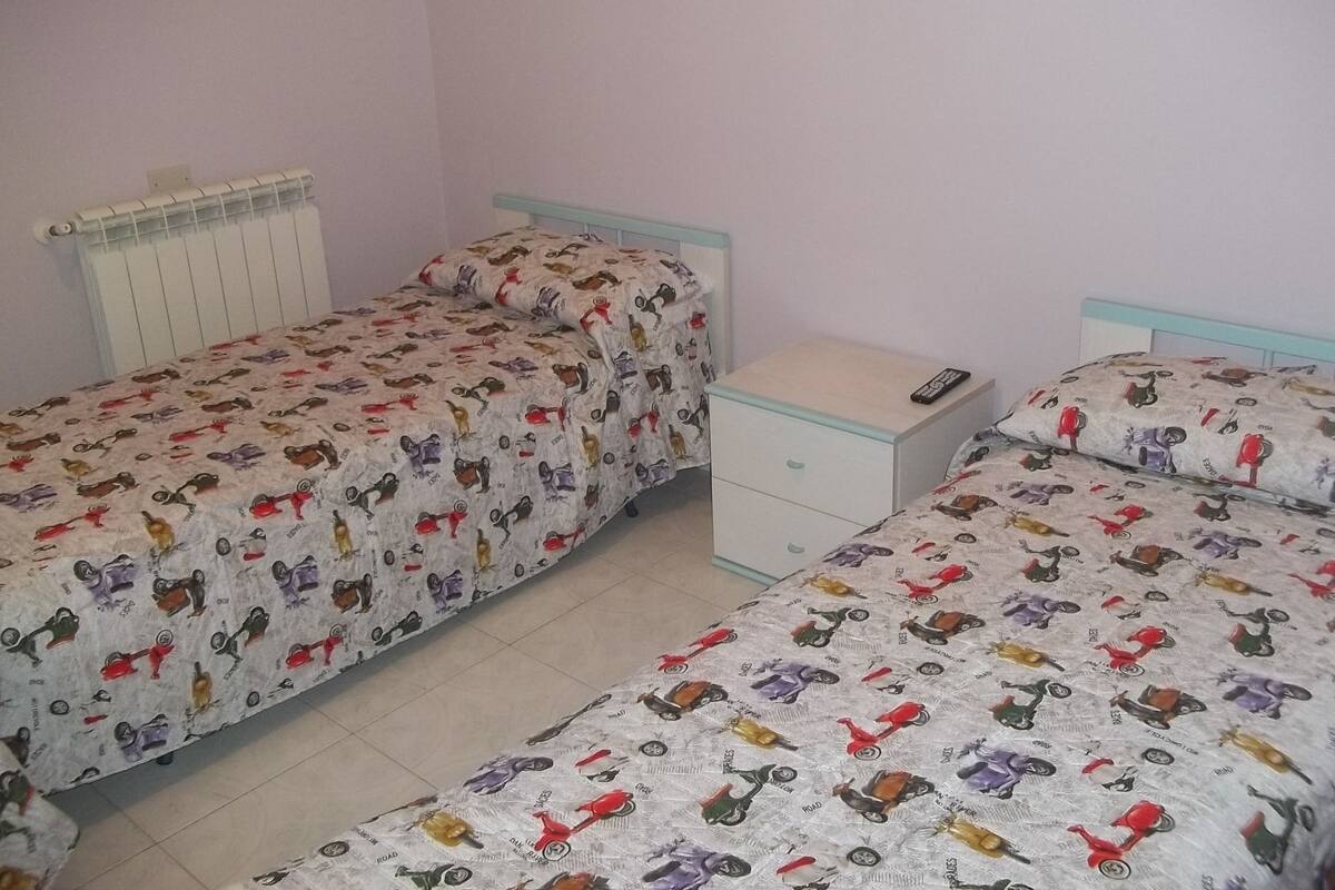 Een slaapkamer met twee eenpersoonsbedden, elk voorzien van een beddengoedovertrek met dessin, een nachtkastje en een radiator aan de muur.