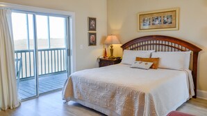 A bedroom with a large bed, a nightstand, a lamp, and a view through a sliding glass door to an outdoor balcony. - The Sunset Inn (Sunset Beach)