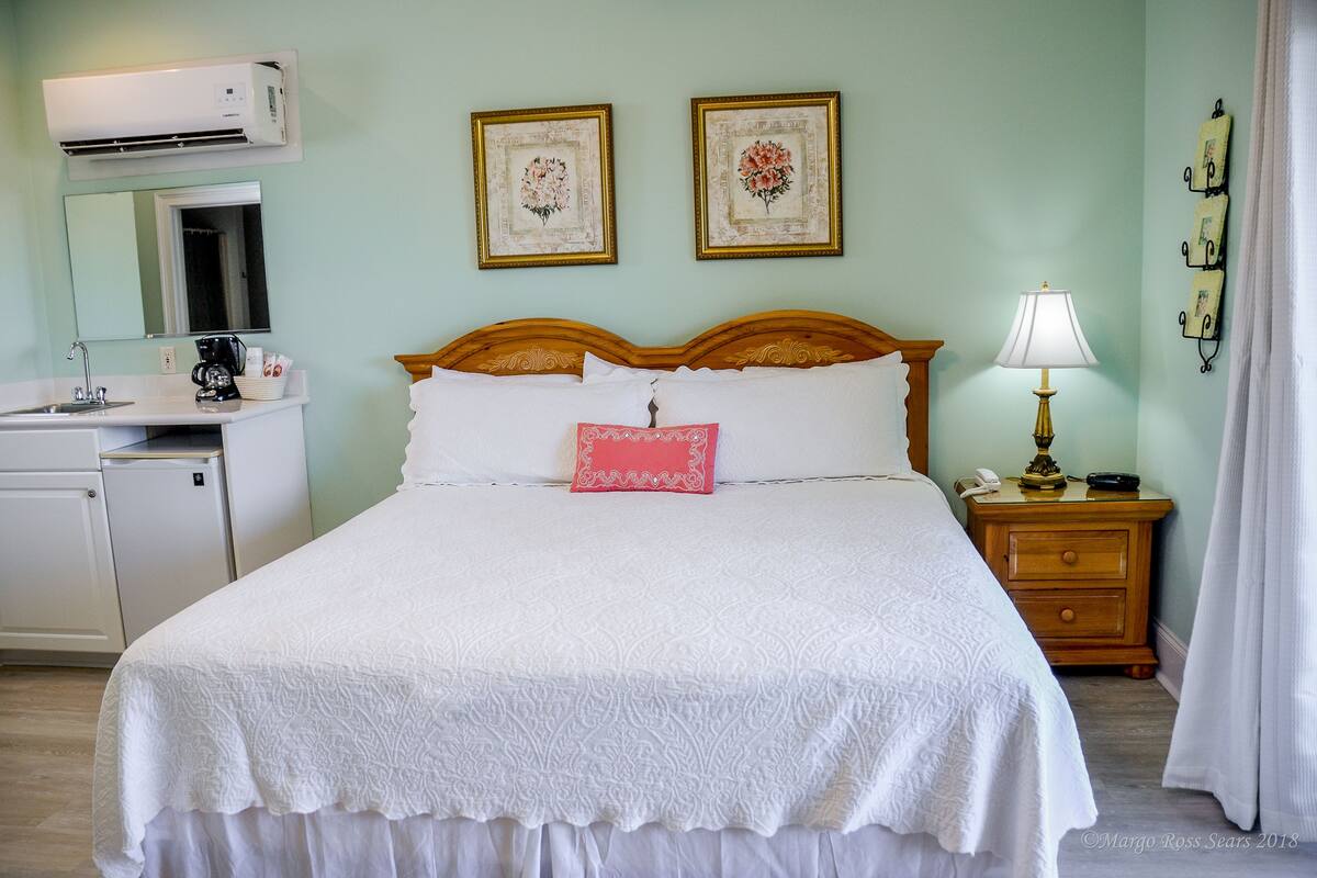 A neatly arranged hotel room with a bed, bedside table, lamp, and a small desk with a coffee maker.