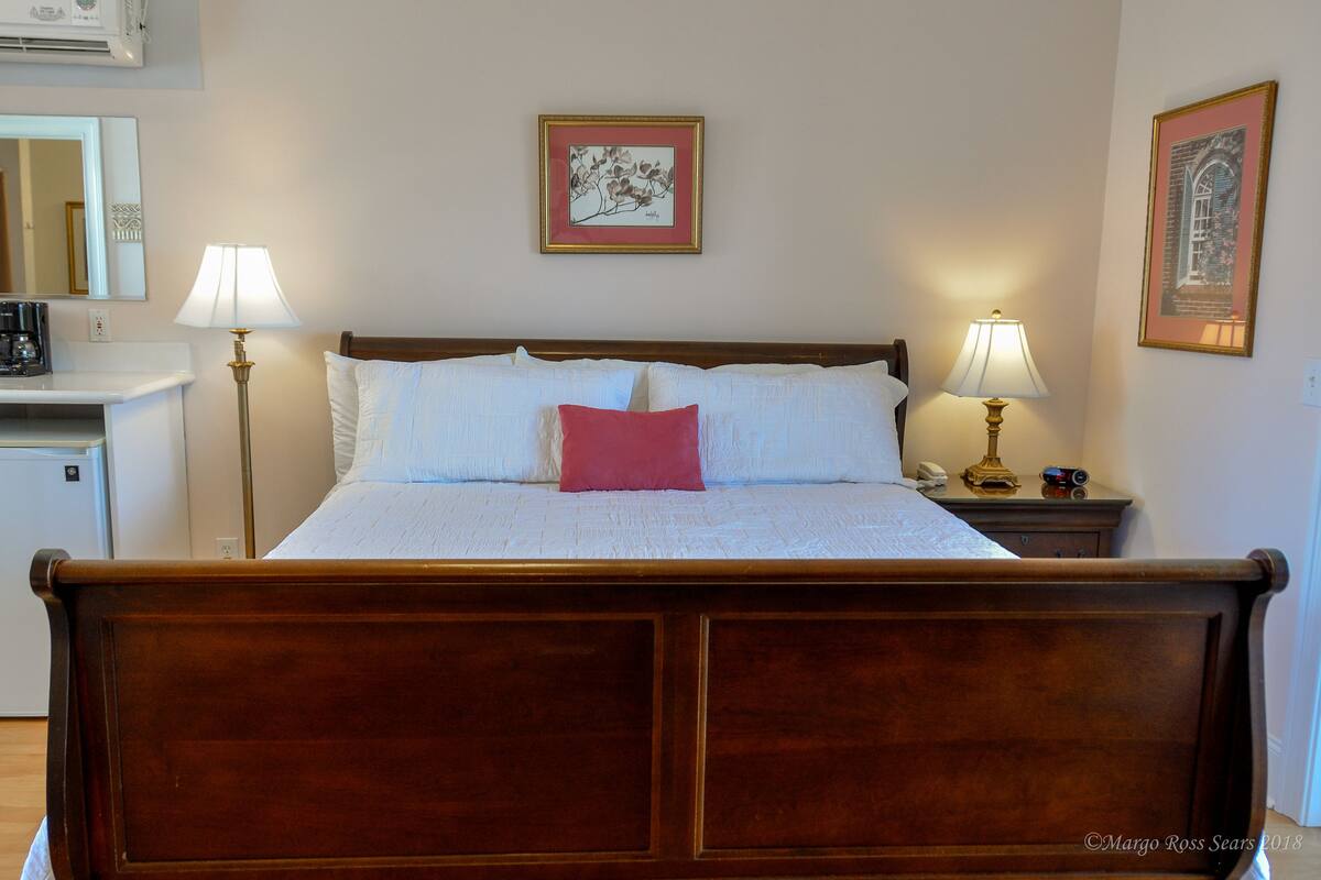 A neatly made bed with white linens and a single red pillow, flanked by two bedside lamps.