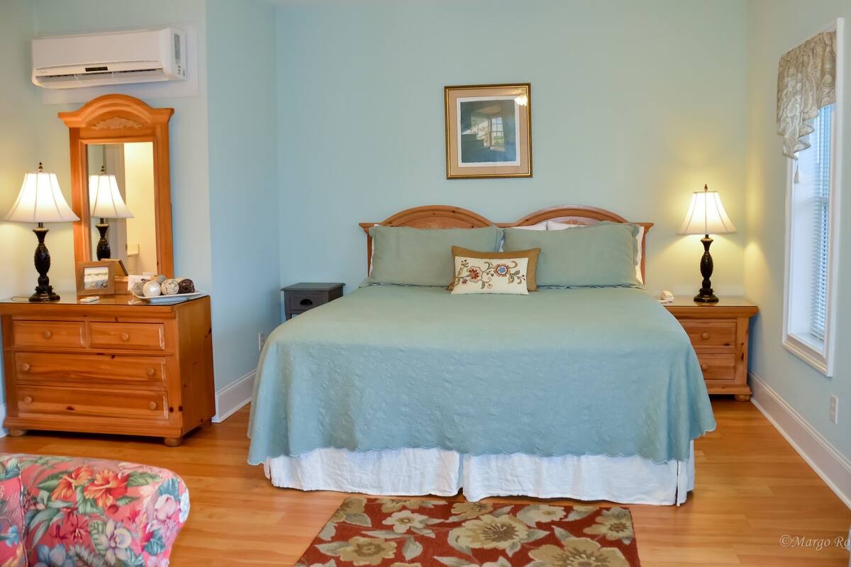 A bedroom with a bed, two bedside tables with lamps, a dresser, a mirror, and a framed picture on the wall.
