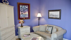 A room with a patterned sofa, a small table with magazines, a lamp, a cabinet, and two framed pictures on the wall. - The Sunset Inn (Sunset Beach)