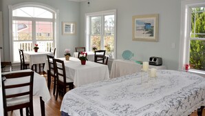 A dining area with white tablecloths, wooden chairs, and a large bed with a patterned bedspread. - The Sunset Inn (Sunset Beach)