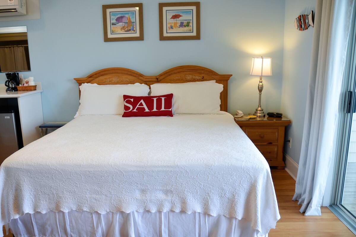 A neatly made bed with a white bedspread and a pillow with the word "SAIL" on it.