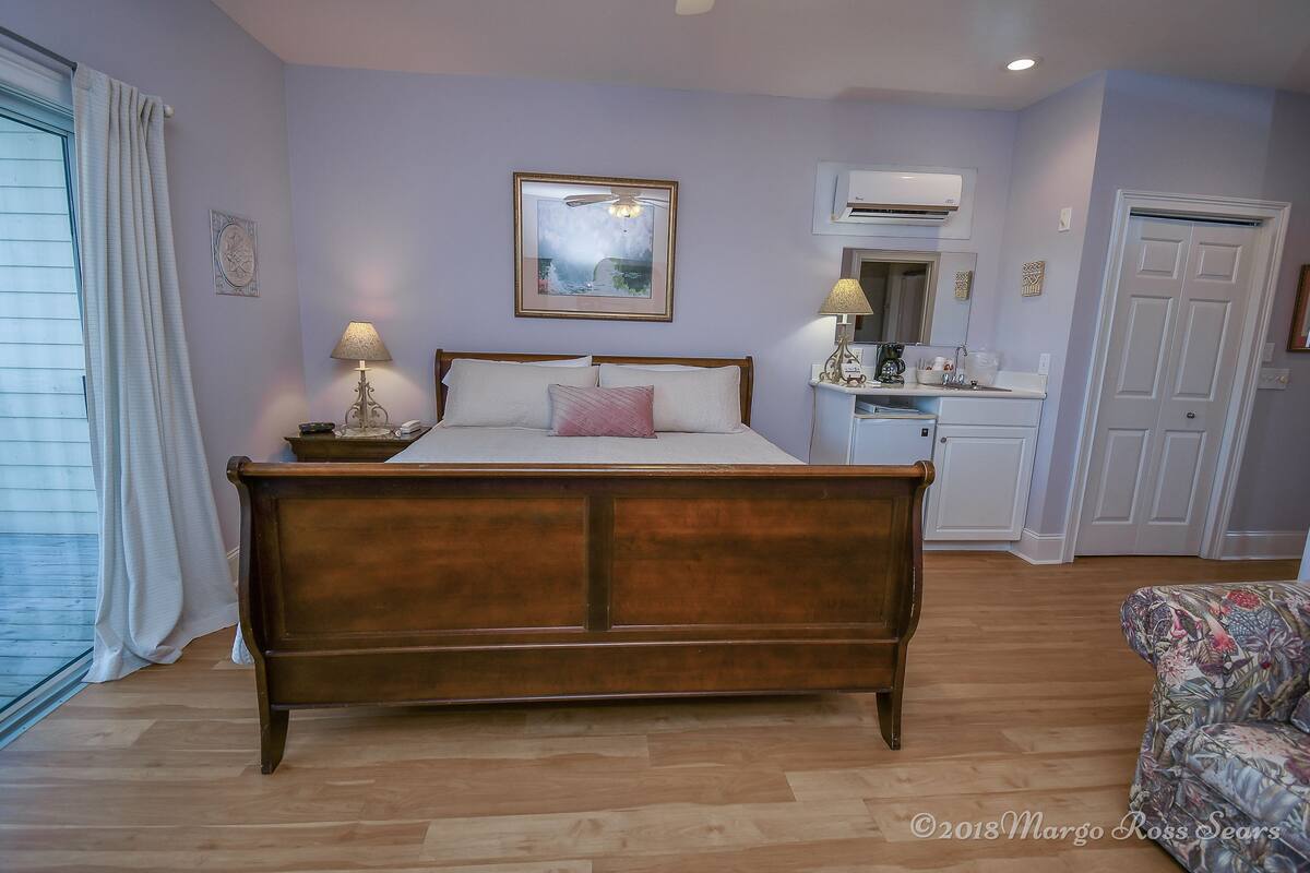 A bedroom with a wooden bed, a nightstand with a lamp, a dresser, and a chair.