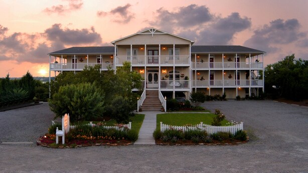 A large, two-story building with a symmetrical facade, multiple balconies, and a central entrance with steps. - The Sunset Inn (Sunset Beach)