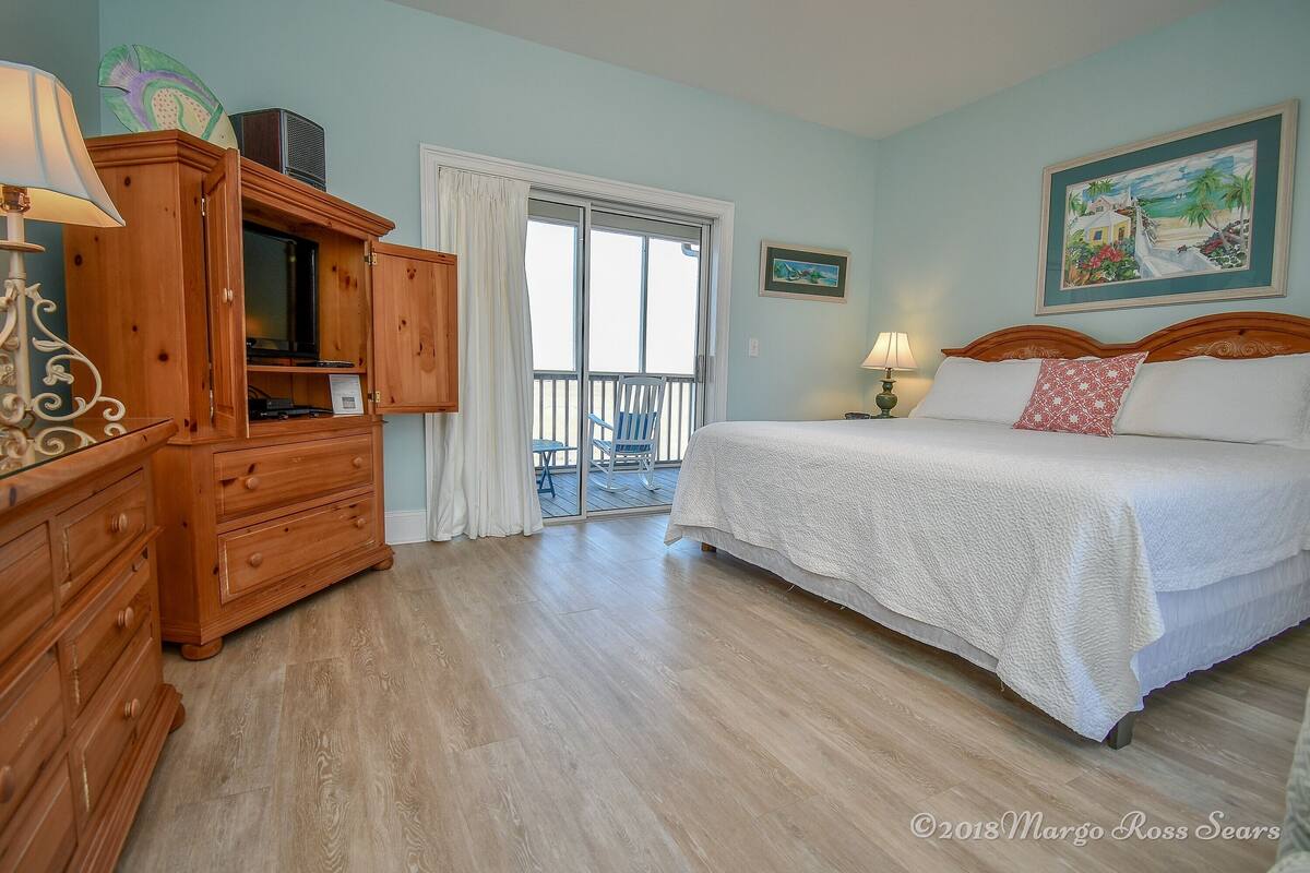 A bedroom with a bed, wooden dresser, and a balcony with a chair.
