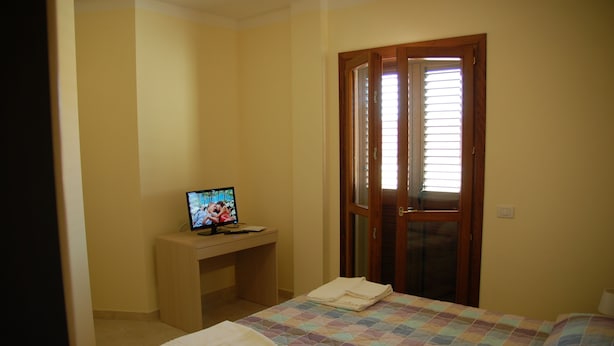 Une chambre à coucher avec un lit, un bureau avec un ordinateur et une porte avec une fenêtre.
