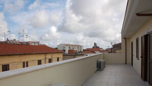 Un balcon doté d’un sol carrelé, d’un climatiseur blanc et offrant une vue sur les bâtiments voisins et une structure en forme de dôme.