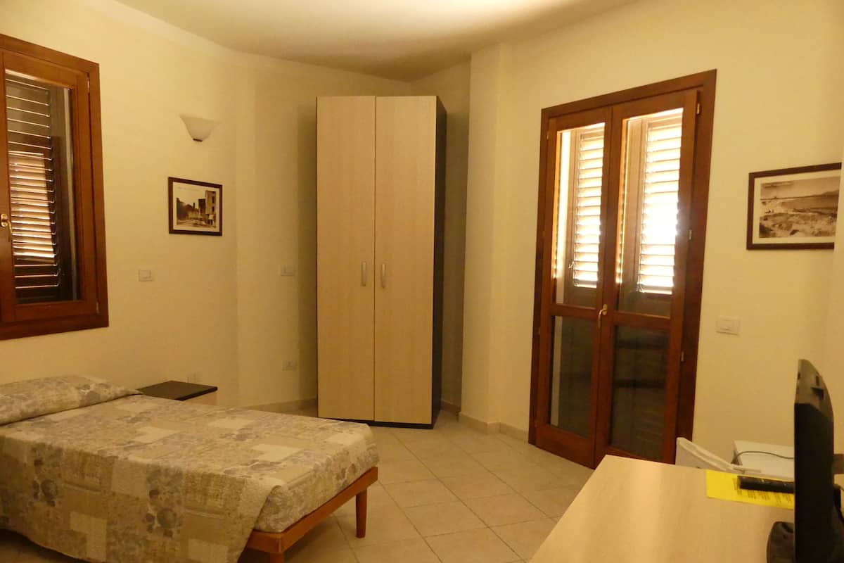 Ein Schlafzimmer mit Bett, Kleiderschrank, Schreibtisch und einer Tür mit Glasscheiben.