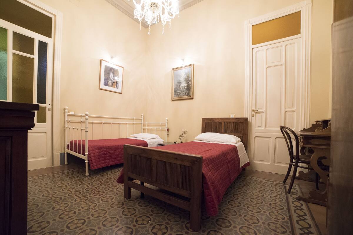 A room with two beds, a chandelier, and a door with a window.