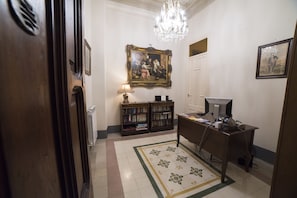 A room with a desk, computer, bookshelves, a chandelier, and a painting on the wall. - Medusa B&B (Palermo)
