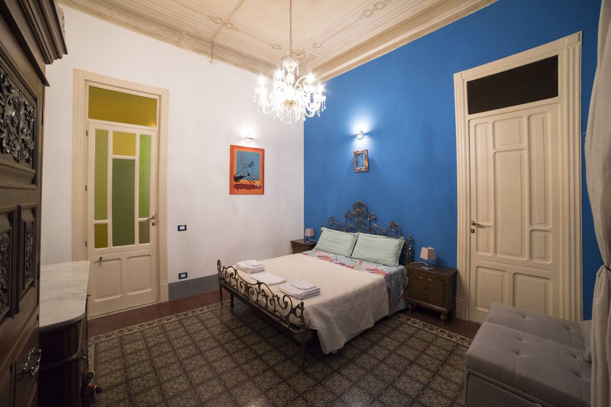 A bedroom with a bed, a nightstand, a dresser, a chandelier, and a door.