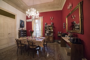 A dining room with a chandelier, a table set for four, and a red wall with a large mirror. - Medusa B&B (Palermo)