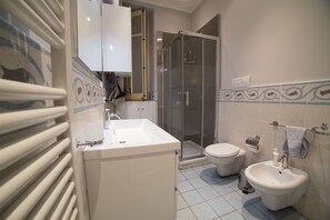 A bathroom with a white sink, toilet, and bidet, a glass shower enclosure, and a towel rack. - Medusa B&B (Palermo)