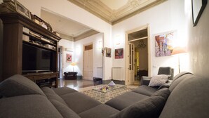 Un salon avec un grand canapé gris, un téléviseur à écran plat et une table basse. Des tableaux encadrés ornent les murs et une lampe se trouve sur la table d’appoint.