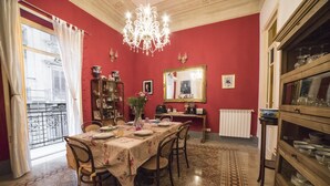 Une salle à manger avec un mur rouge, un lustre, un buffet en bois et une vue sur la ville par une fenêtre.