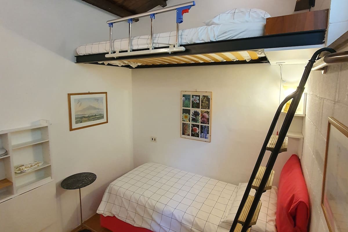 Une petite pièce avec un lit superposé, un ventilateur de plafond, une petite table et une échelle.