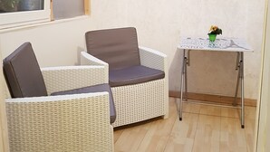 A corner room with a wicker sofa, a small table with a potted plant, and a sunset painting on the wall. - Affittacamere Maristella (Cagliari)