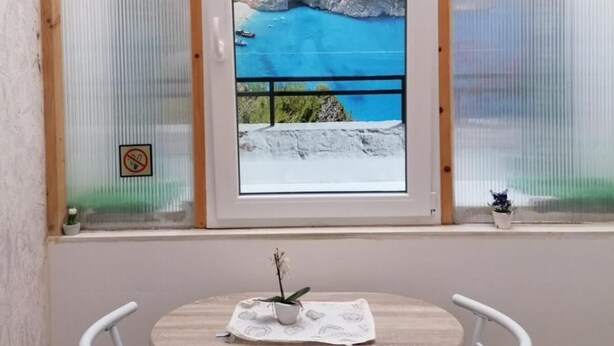 A room with a window overlooking a coastal landscape, a small table with a chair, and a potted plant on the windowsill. - Affittacamere Maristella (Cagliari)