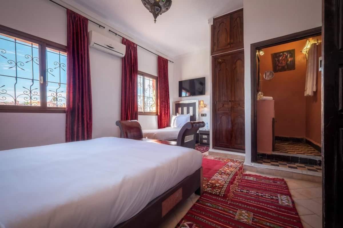 A hotel room with a large bed, a desk with a chair, a TV, and a bathroom with a shower.