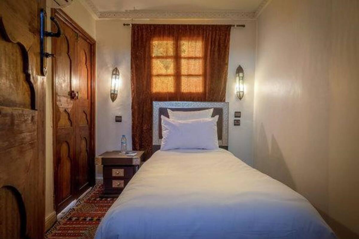A hotel room with a bed, a nightstand, a wooden wardrobe, and a window with curtains.
