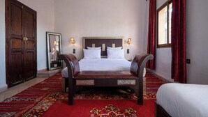 Habitación de hotel con una cama grande, un banco de madera, una alfombra roja y un espejo amplio.