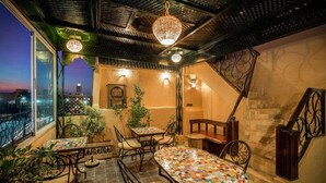 Un área de comedor exterior acogedora con una mesa de mosaico, sillas y una escalera que lleva a un nivel superior.
