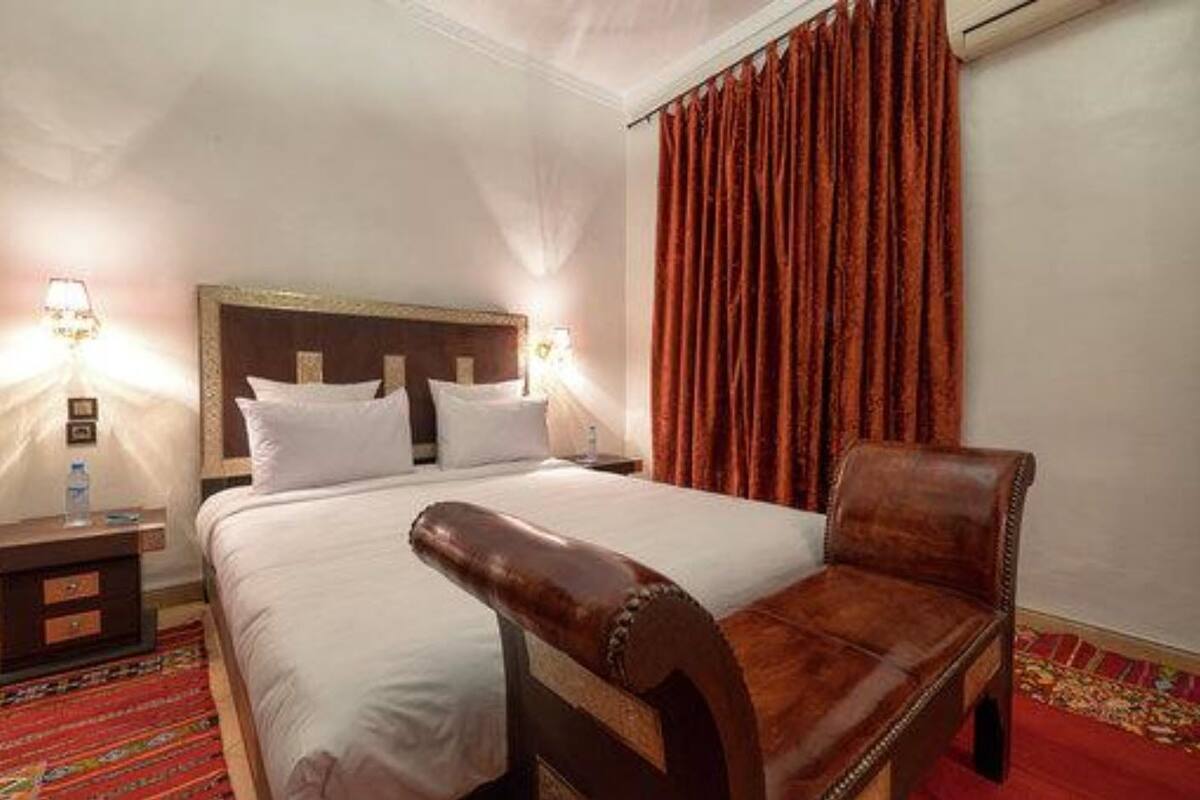 A hotel room with a large bed, two bedside tables, a wooden chair, a red curtain, and a patterned carpet.
