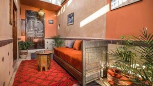 Un pasillo estrecho con alfombra roja estampada, un sofá, una mesita y un muro decorativo con una puerta y un cuadro enmarcado.