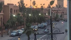 Vista callejera al atardecer con edificios, coches y una mezquita al fondo.