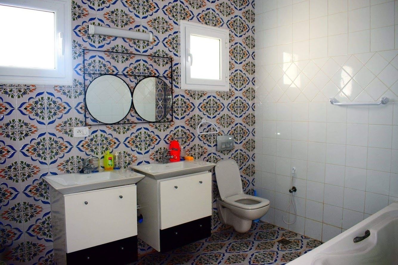 A bathroom with patterned tiles, a toilet, a sink with a mirror, and a bathtub.