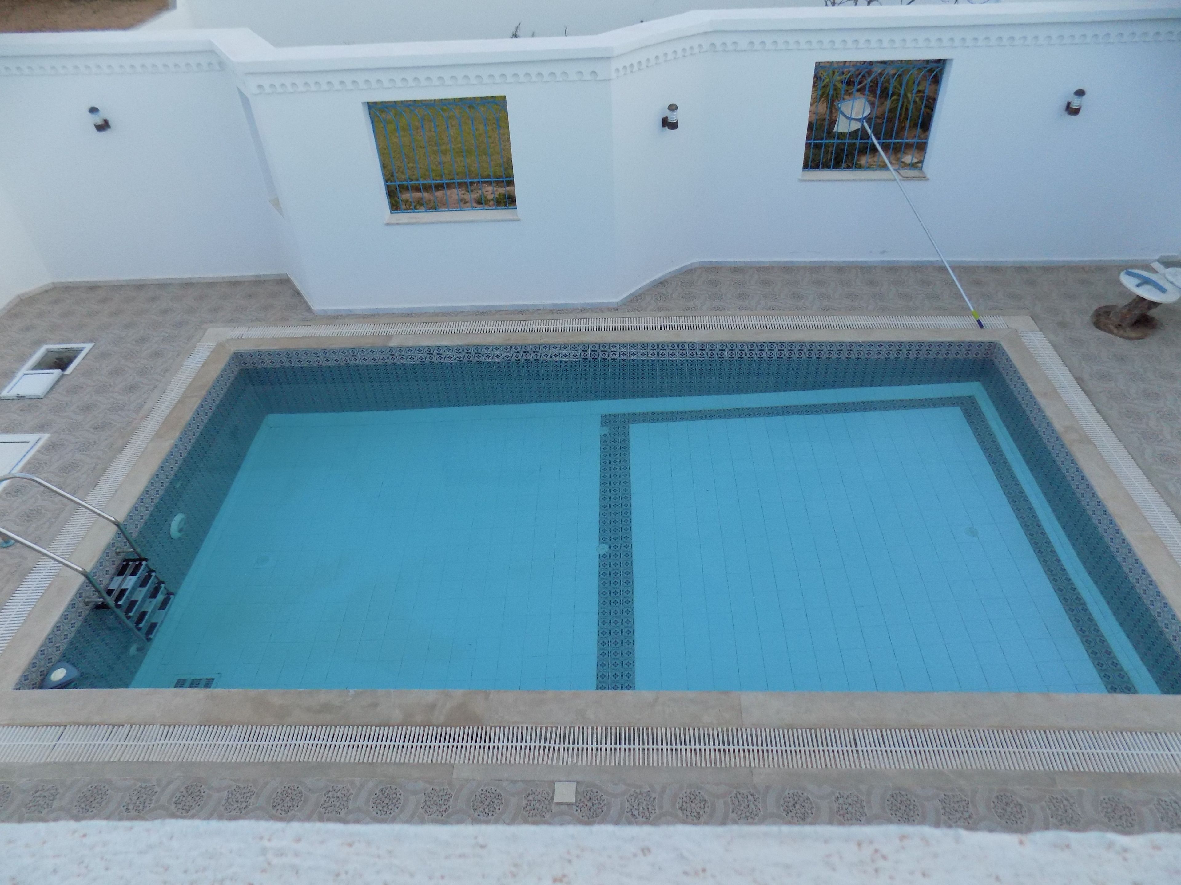 Ein rechteckiger Pool mit gefliestem Rand, einer Leiter und einem kleinen Fenster mit Metallgitter.