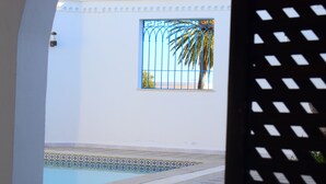 A pool area with a tiled border, a window with a palm tree outside, and a white wall. - House Dar Mamina (Zarzis)