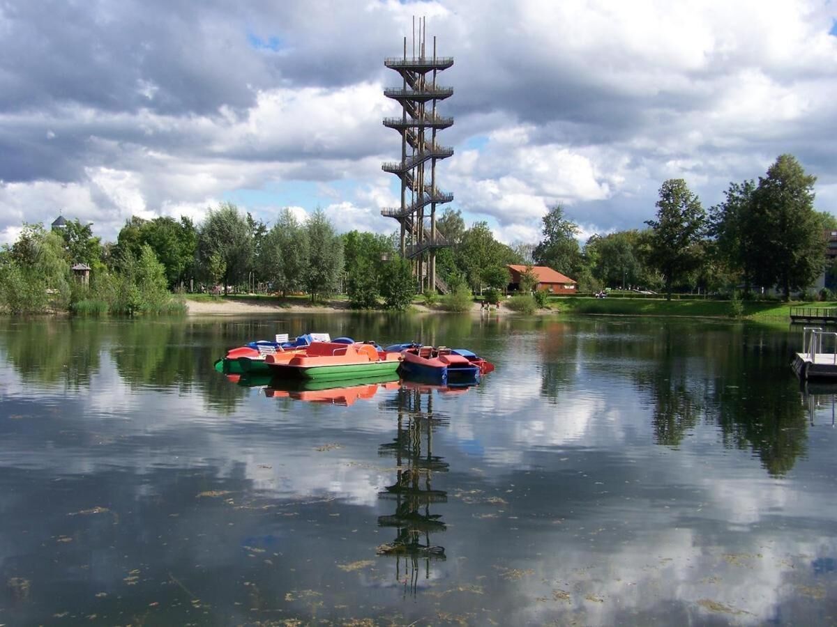 Un lago tranquilo con barcos y una alta estructura de torre al fondo.