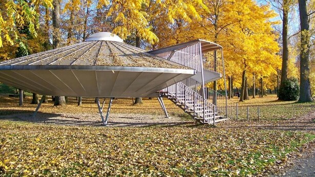 Ein Pavillon mit Dach und Treppe, umgeben von Bäumen mit gelben Blättern.