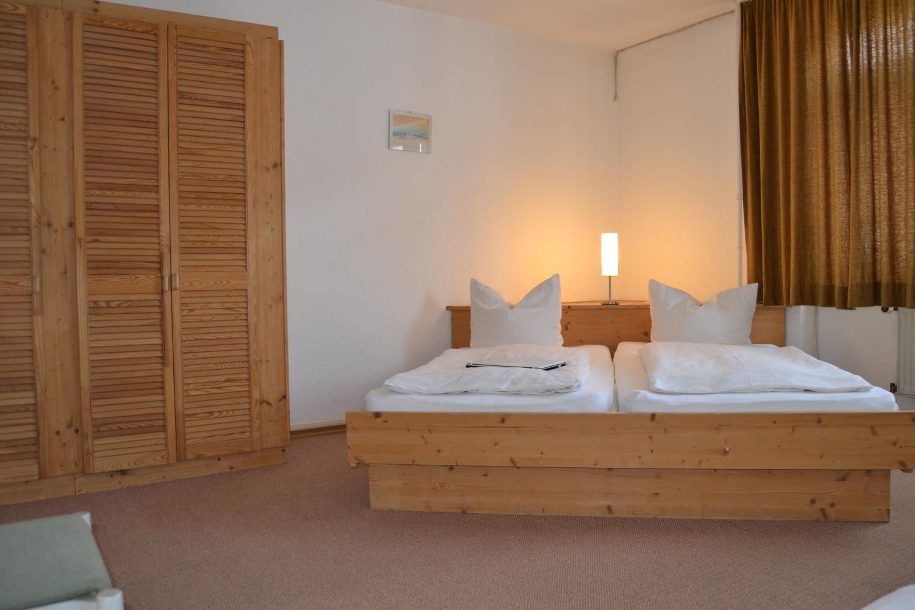 A bedroom with a wooden bed, a nightstand, a lamp, and a window with curtains.
