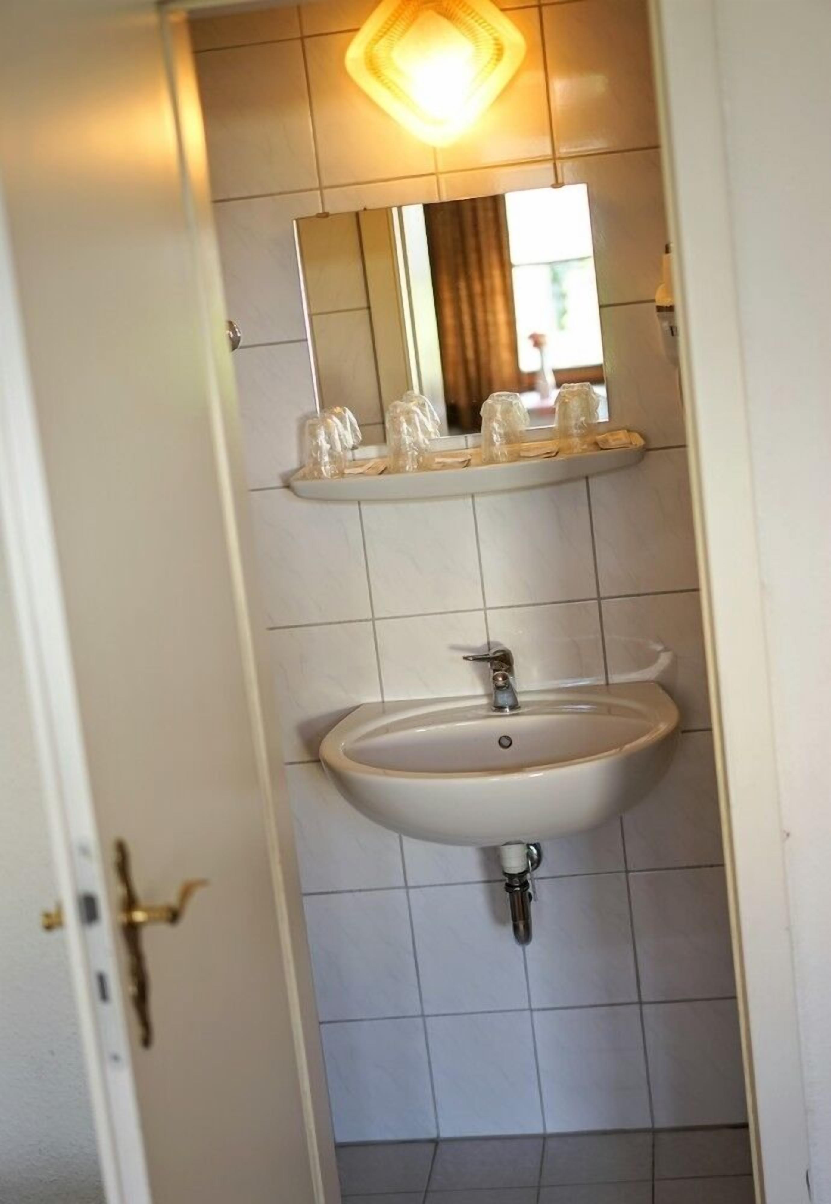 A bathroom with a white sink, a mirror, and a shelf with toiletries.