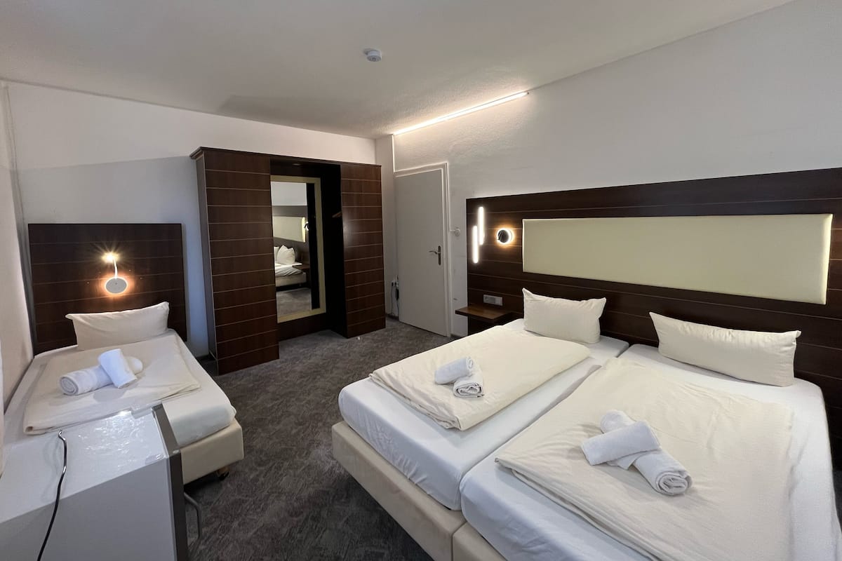 Quarto de hotel com duas camas, uma escrivaninha, um espelho e um banheiro visível por uma porta aberta.