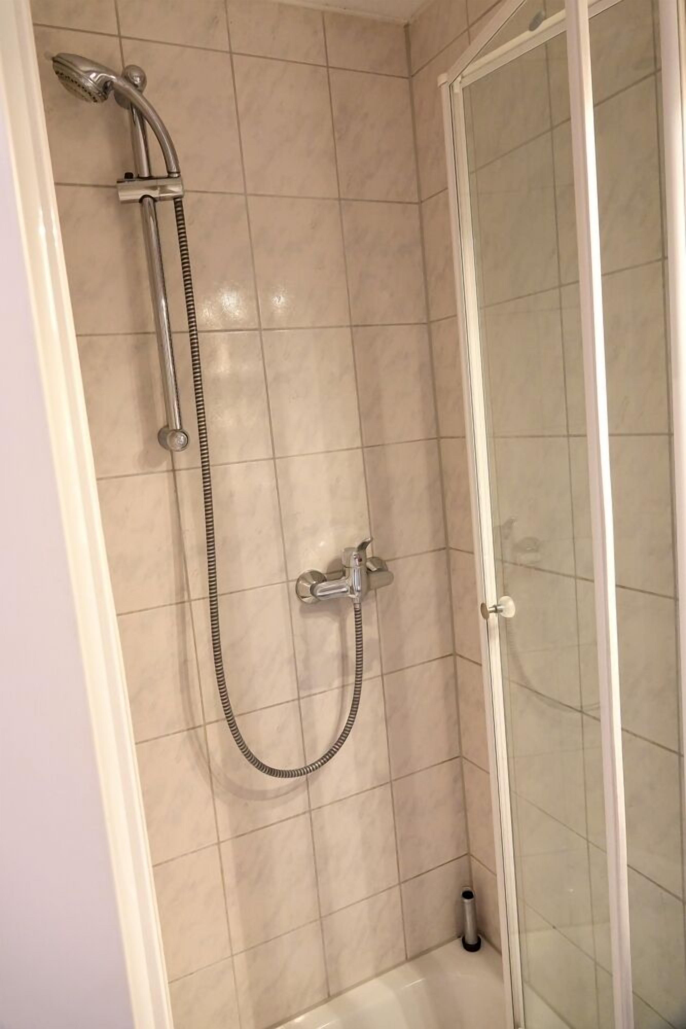 A shower area with a glass door, a handheld showerhead, and a wall-mounted faucet.